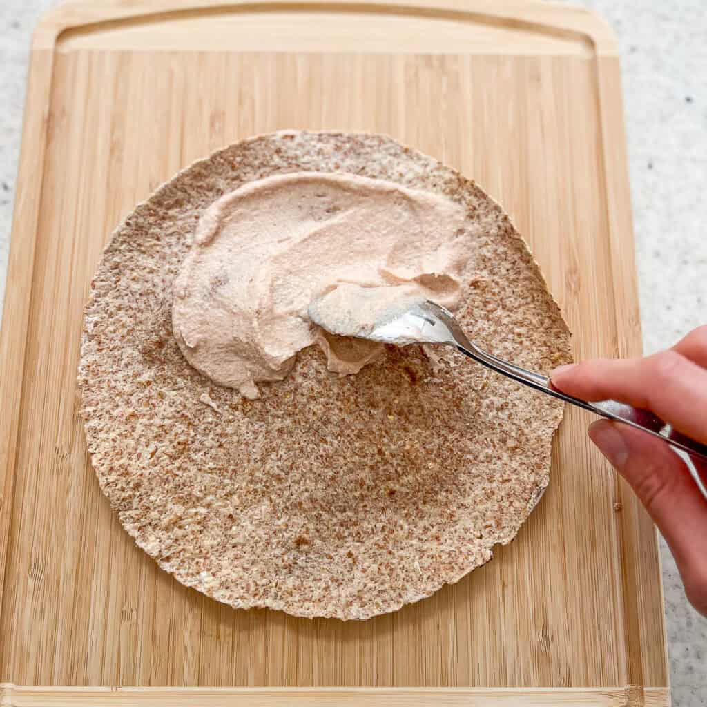 Sweet cashew cream being spread on a toasted sprouted grain tortilla crust.