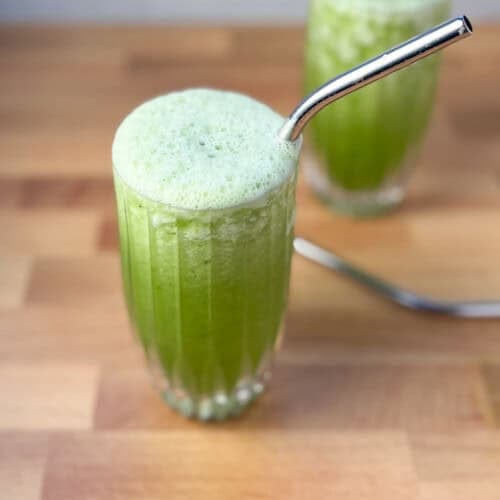 A frosty celery smoothie in glass with metal straw; another smoothie blurred in the background.