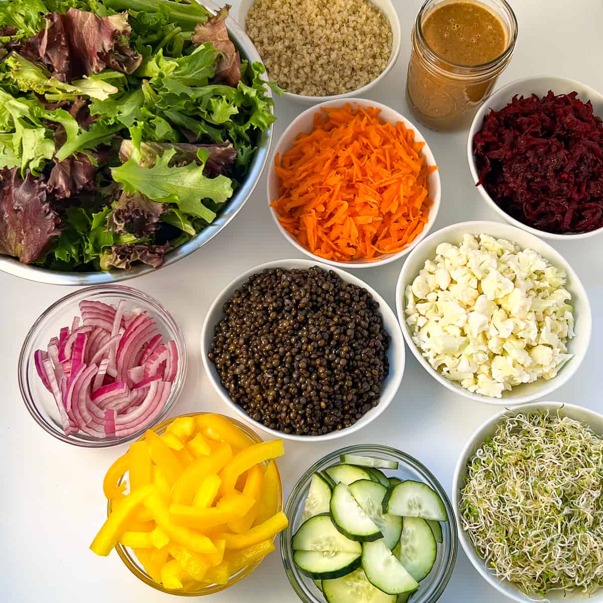 top view of superfood salad ingredients: lettuce greens, quinoa, walnut dressing carrots, beets, cauliflower, lentils, onion, bell pepper, cucumbers, sprouts
