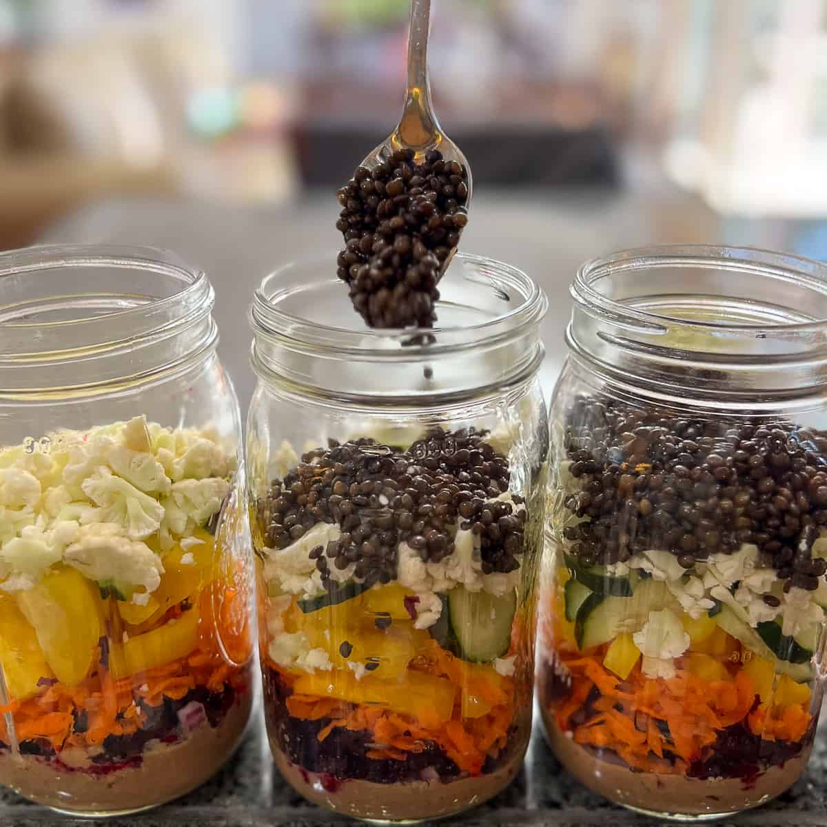 black lentils being spooned into mason jars with veggies
