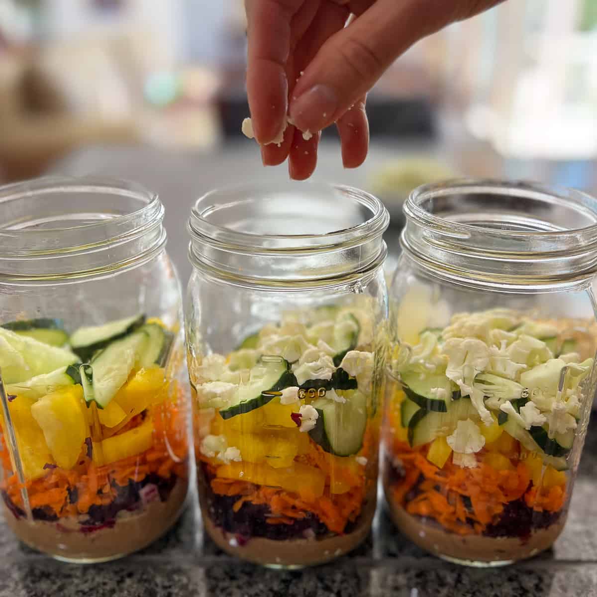 woman's hand adding chopped cauliflower to mason jar of other veggies