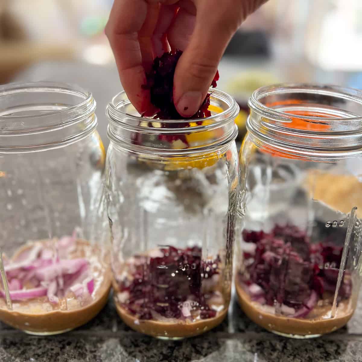 woman's hand adding shredded beet to mason jars