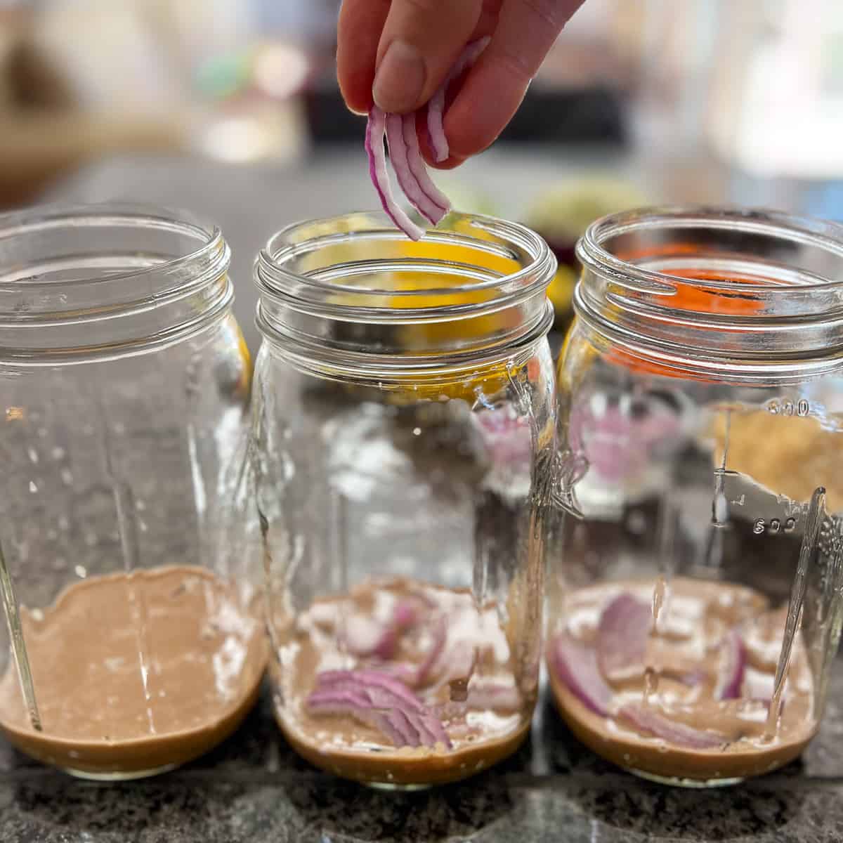woman's hand adding chopped onion to mason jar with dressing