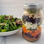 side view close up of superfood salad in a mason jar with a bowl of mixed baby salad greens on the side