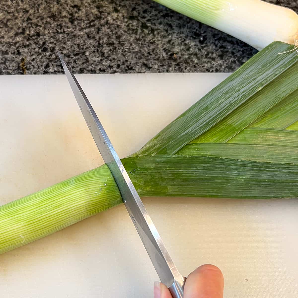 top view of leek on a cutting board with a knife cutting the tops off