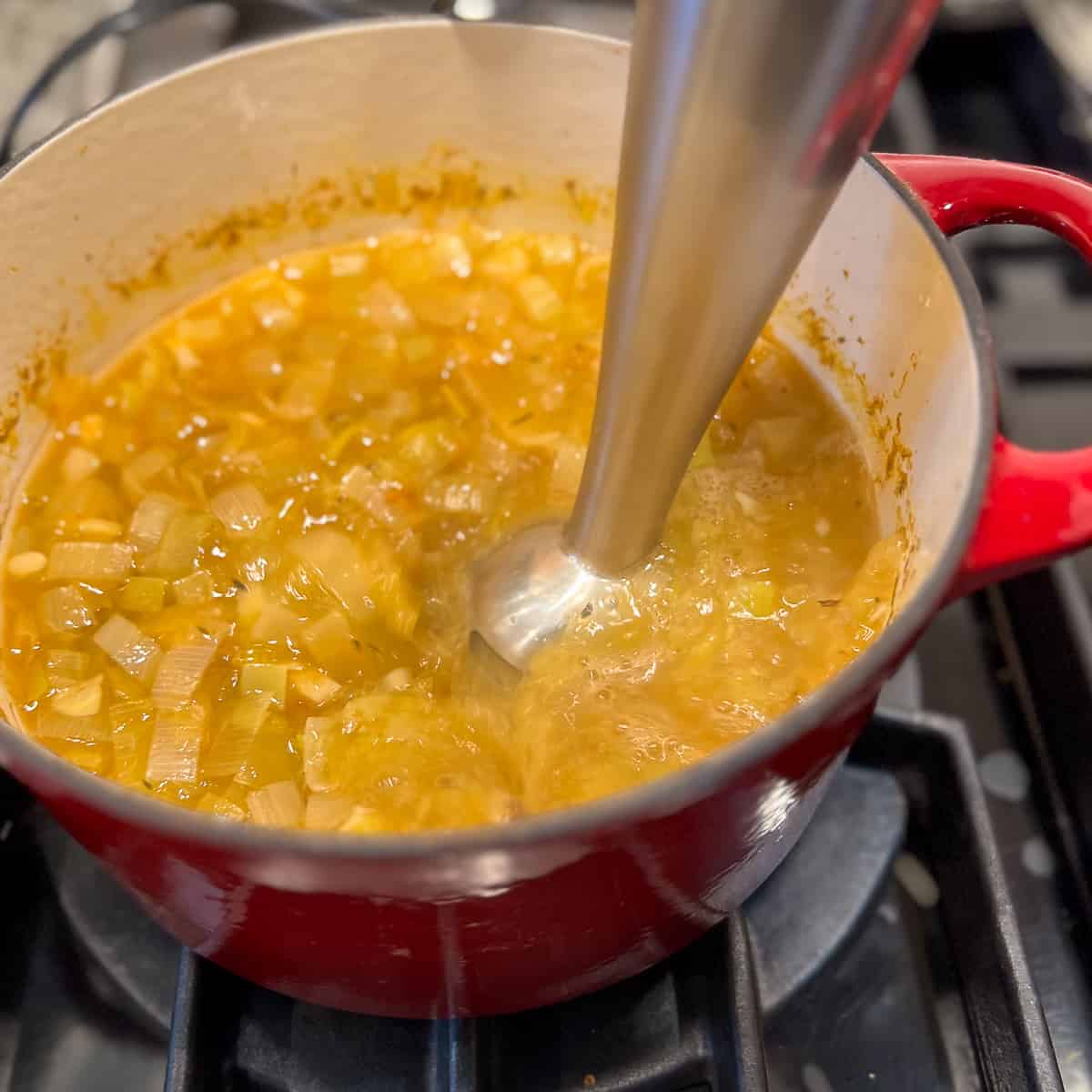 an immersion blender blending the soup on the stovetop