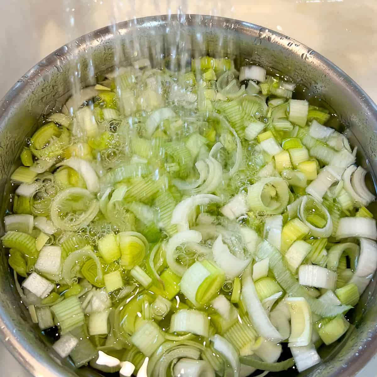 top view of a bowl of chopped leeks being rinsed in the sink under running water