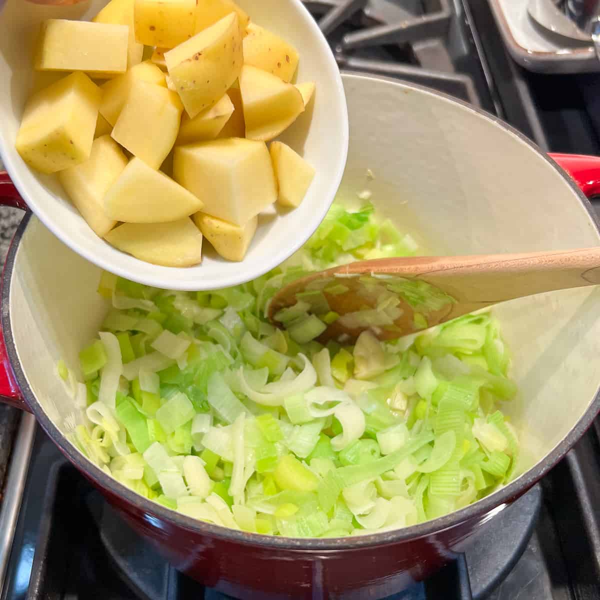 top view of potatoes being added to the pot with leeks and garlic on the stovetop