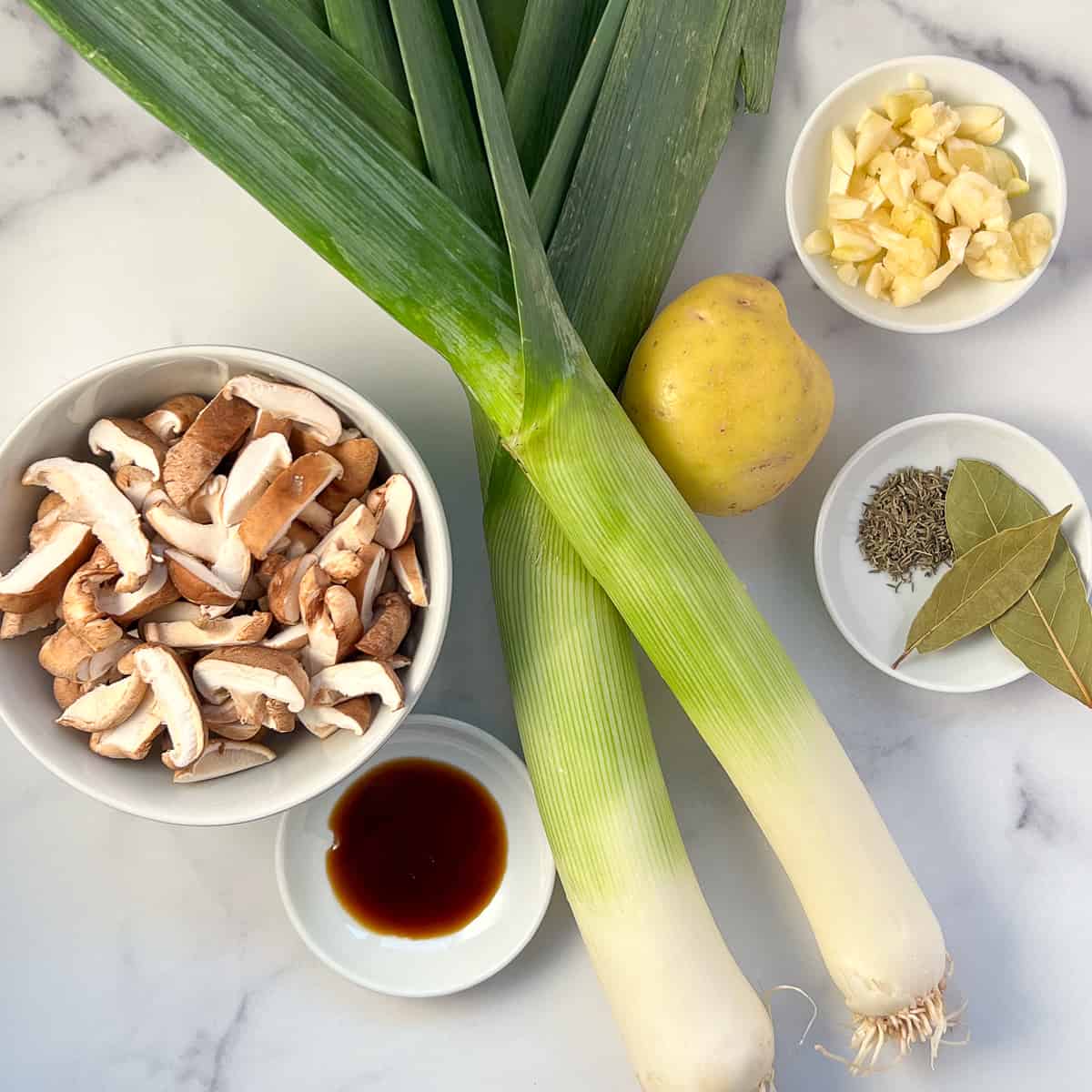 top view of key ingredients for leek and mushroom soup: leeks, chopped mushrooms, chopped garlic, potato, spices and coconut aminos