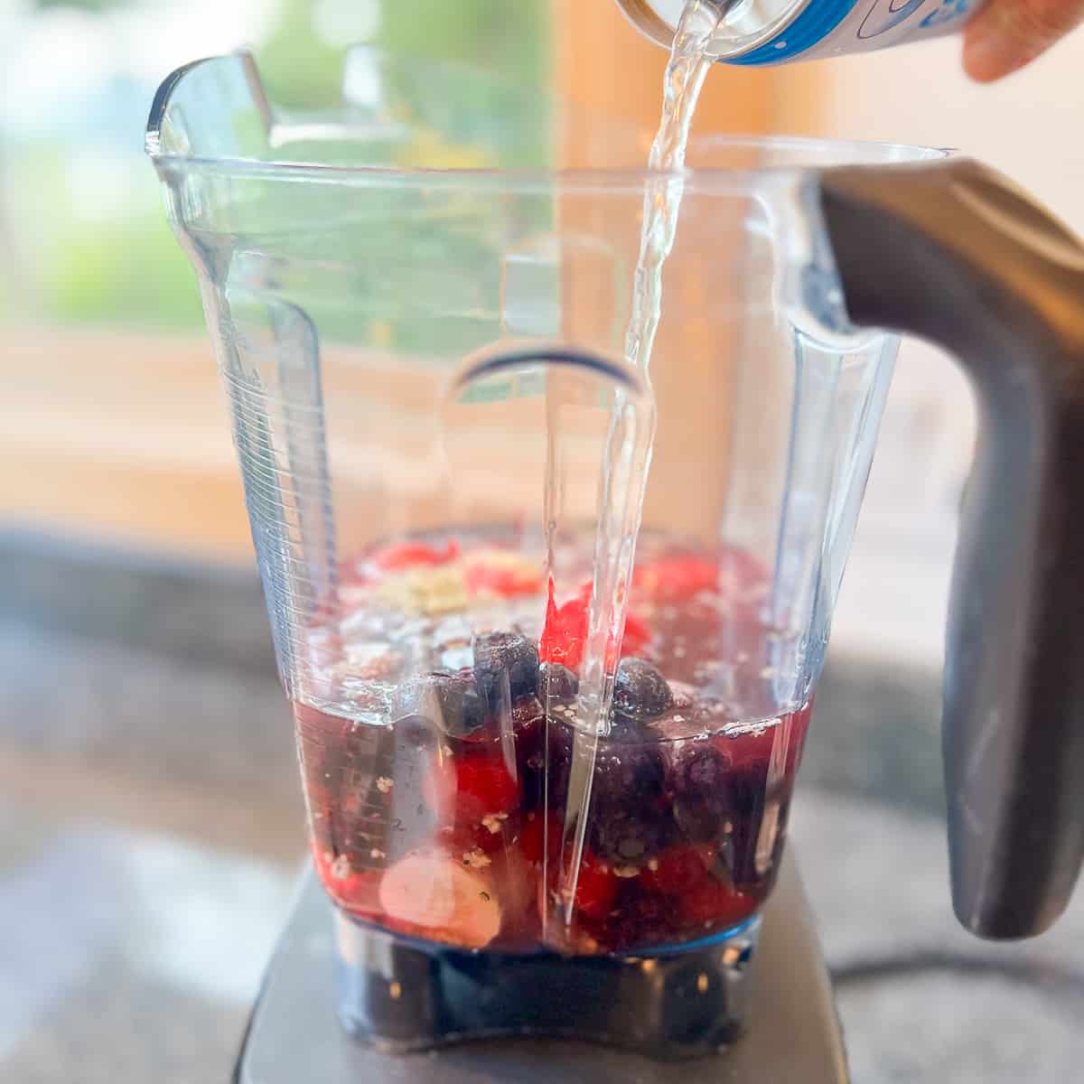 side view of fruit in a blender with coconut water being poured in