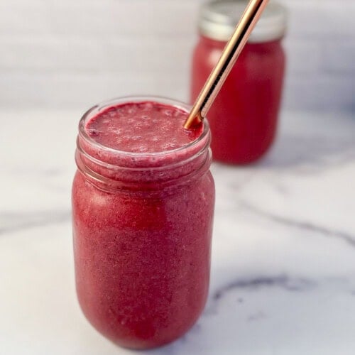 A mixed berry smoothie in mason jar with metal straw.