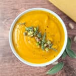 top view of a bowl of vegan butternut squash soup topped with fresh sage, pistachios, and black pepper