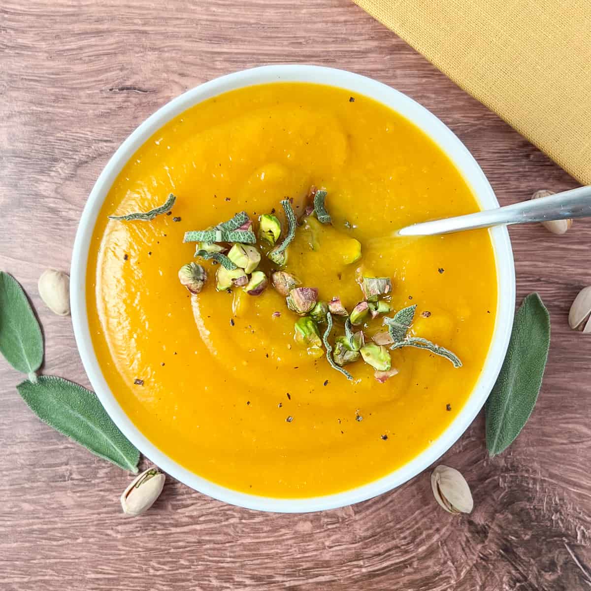 top view of a bowl of butternut squash soup topped with chopped pistachios and fresh sage