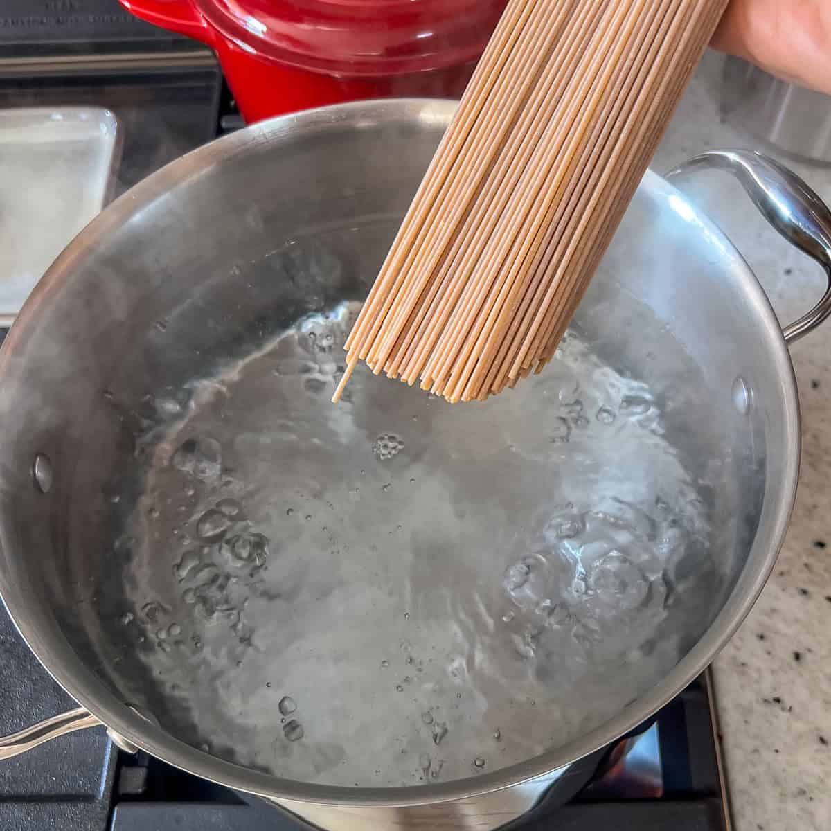 Whole wheat spaghetti pasta being added to a pot of boiling water.
