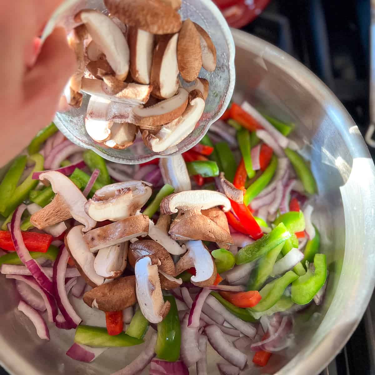 top view of mushrooms being added to a saute pan with veggies on the stovetop