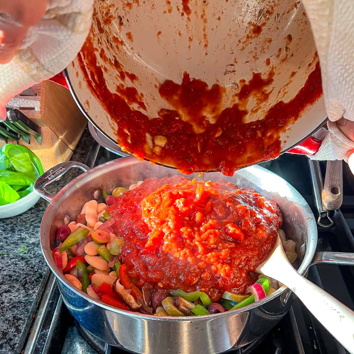 side top view of tomato sauce being added to a large saute pan with veggies and butter beans