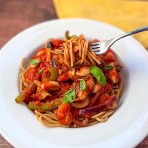 A bowl of vegan puttanesca over spaghetti with a fork of pasta sticking out.