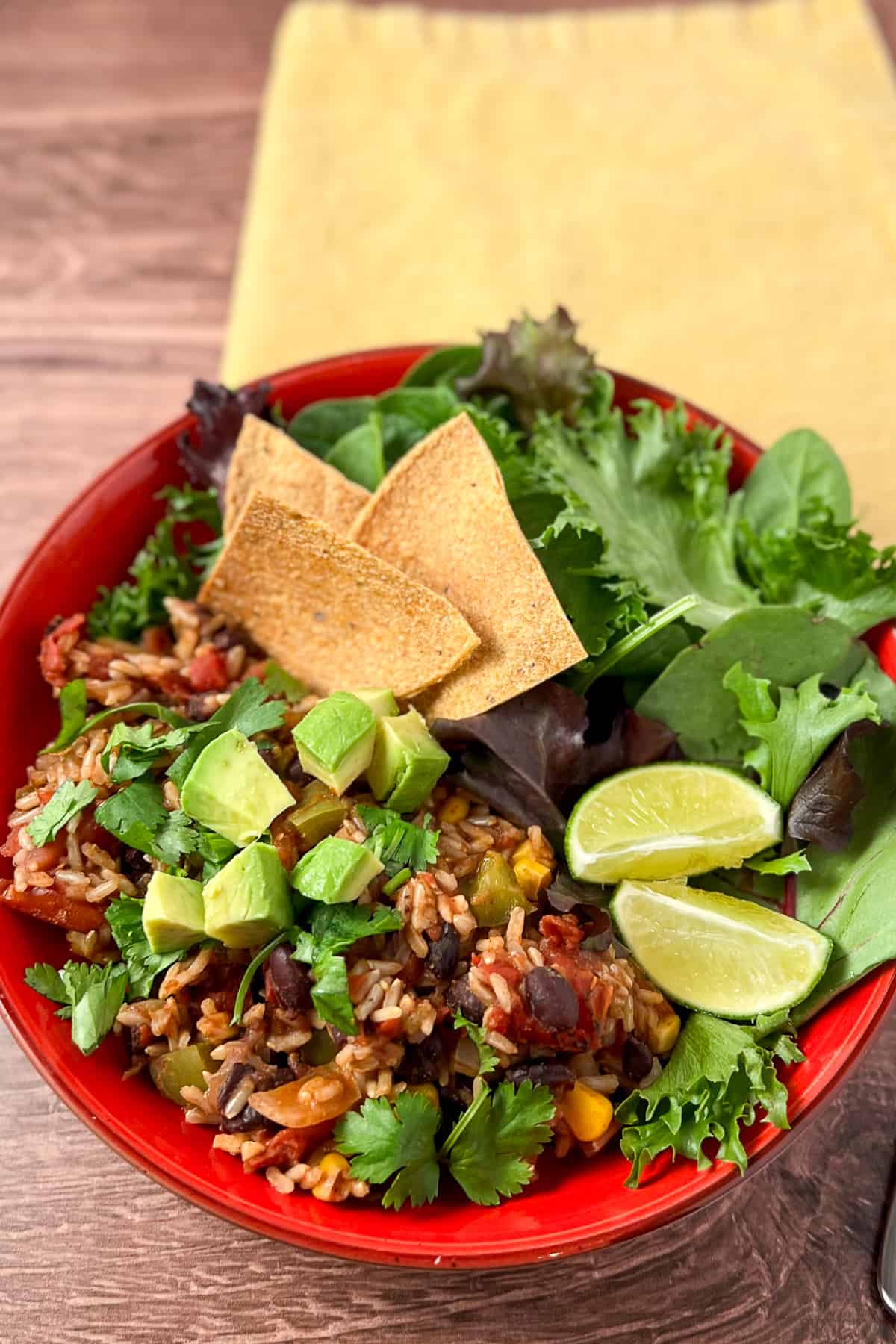 top view of Mexican Rice Casserole with avocado, cilantro, lime, green salad and oven baked tortilla chips