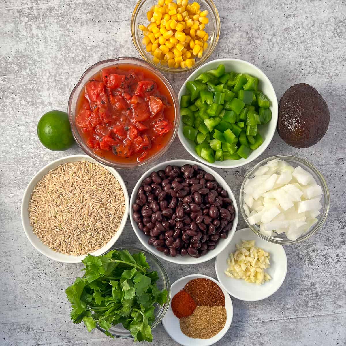 top view of ingredients for mexican rice casserole: rice, beans, bell pepper, onions, garlic, spices, cilantro, avocado, lime, diced tomatoes