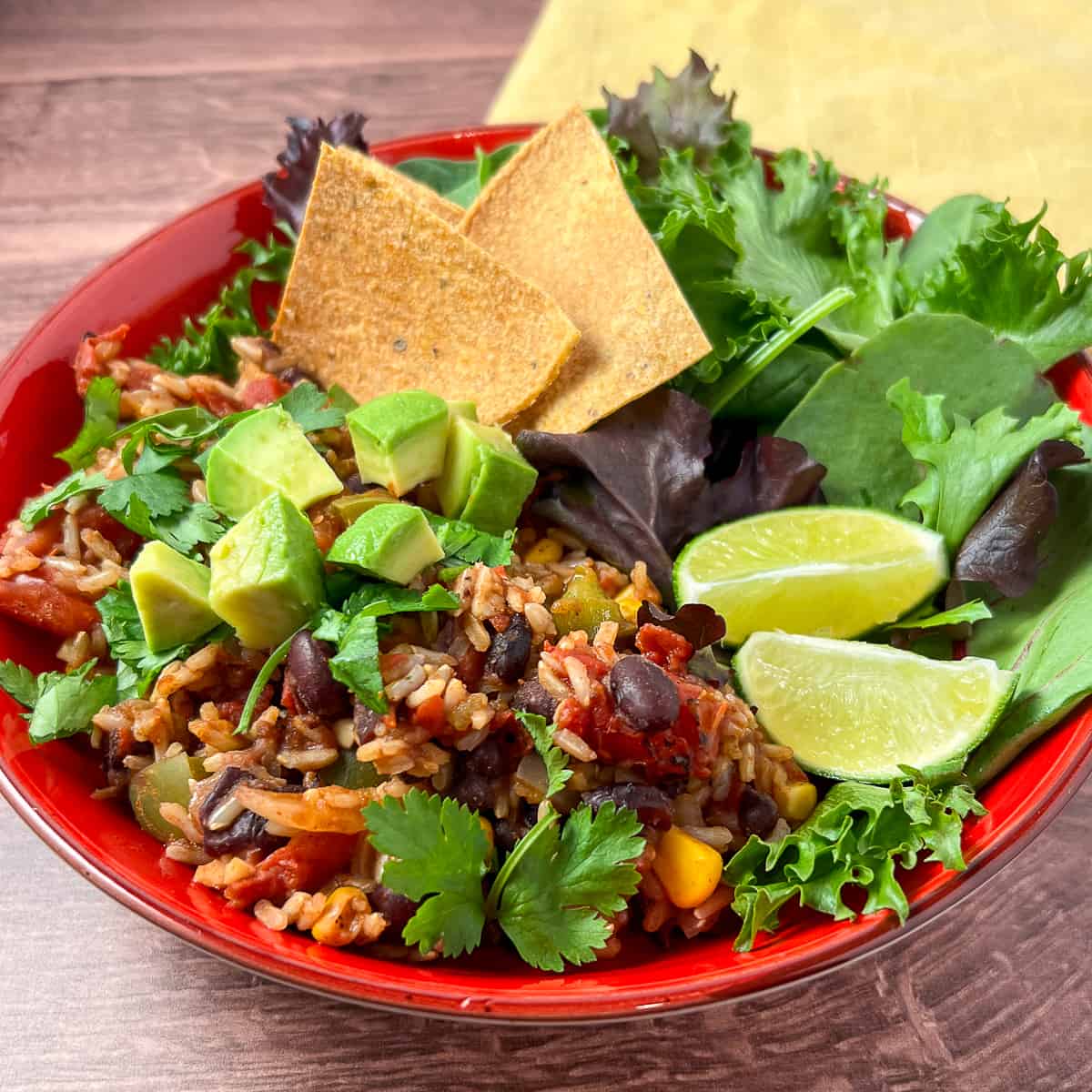 top view close up of Mexican Rice Casserole in a bowl topped with diced avocado, fresh cilantro, lime, oven-baked tortilla chips and side green salad