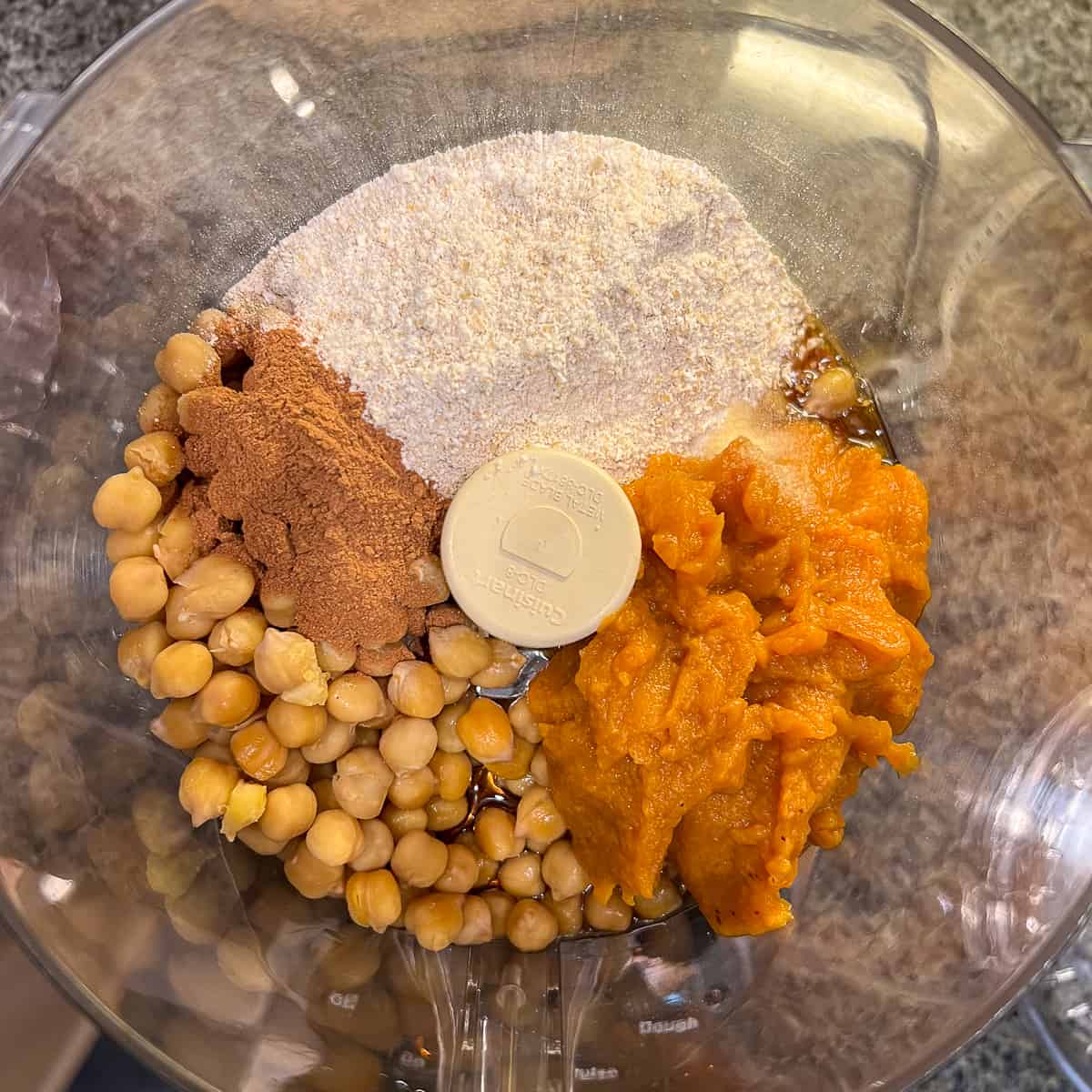 top view of a food processor with chickpeas, pumpkin puree, maple syrup, pumpkin pie spice, ground rolled oats