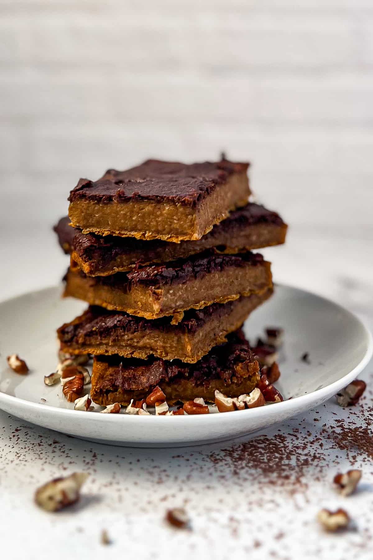 side view of stacked pumpkin brownies with chocolate topping and chopped pecans scatter on and around the plate