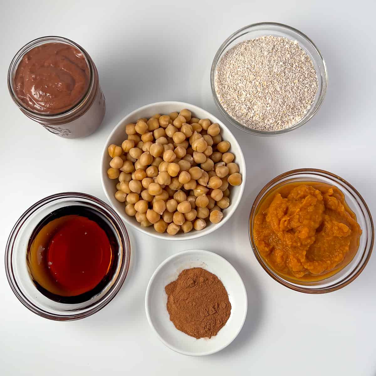 top view of ingredients for pumpkin brownies: chickpeas, ground rolled oats, pumpkin puree, pumpkin pie spice, maple syrup, and chocolate tahini sauce