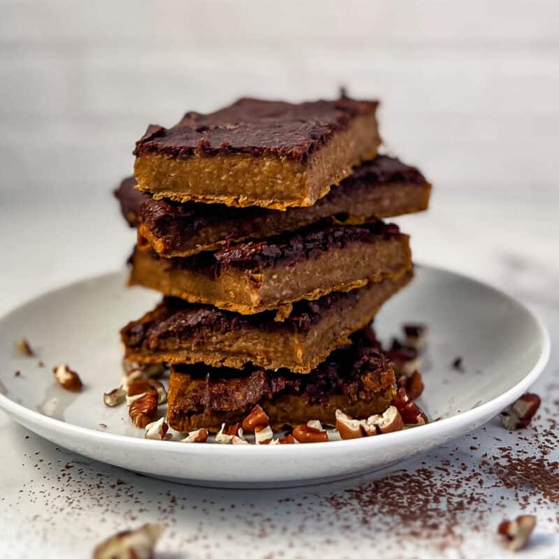 side view of stacked pumpkin brownies with chocolate topping and chopped pecans scatter on and around the plate