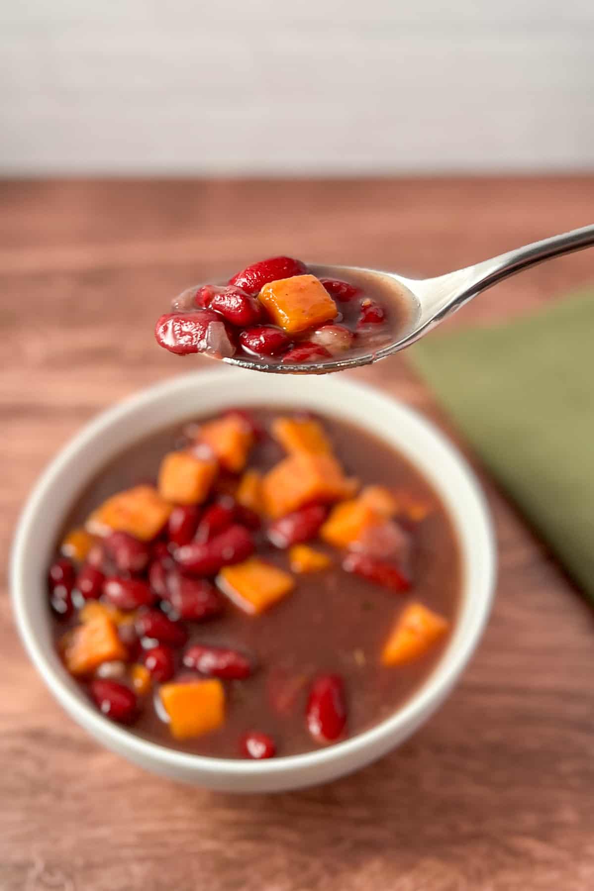 a spoon lifted with bean soup; bowl of kidney bean soup blurred in the background
