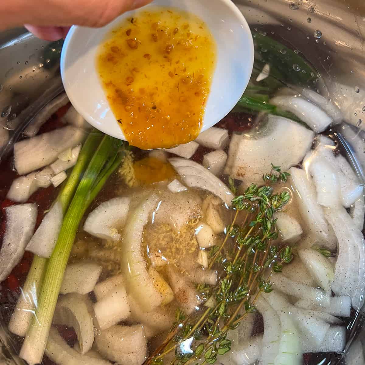 top view of sauce being added to the Instant Pot with beans, water, onion, and herbs
