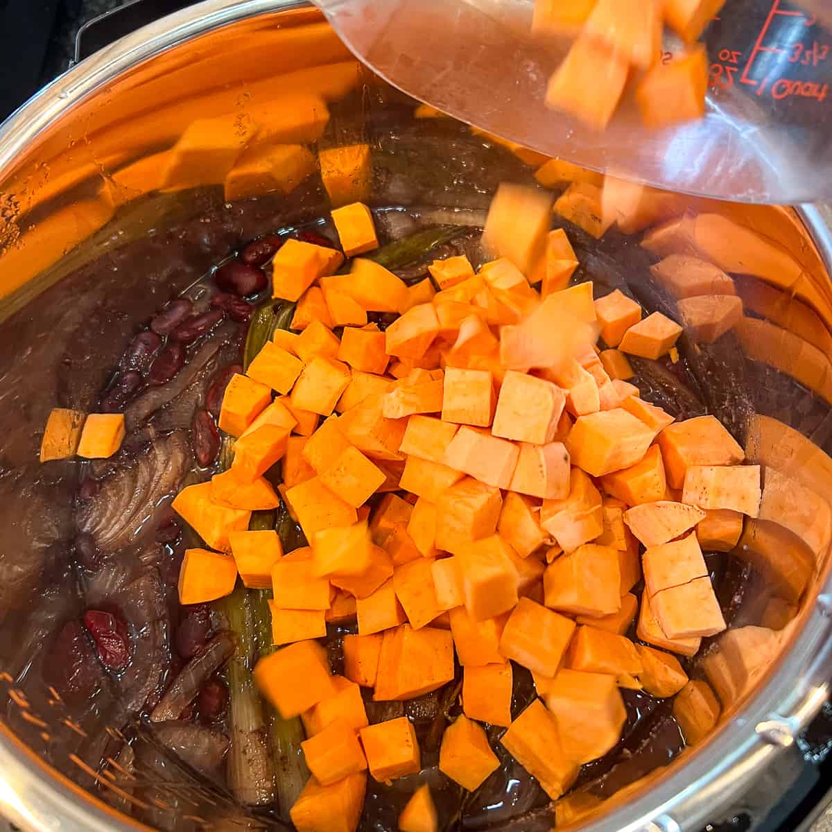 top view of chopped sweet potatoes being added to the Instant Pot with cooked beans