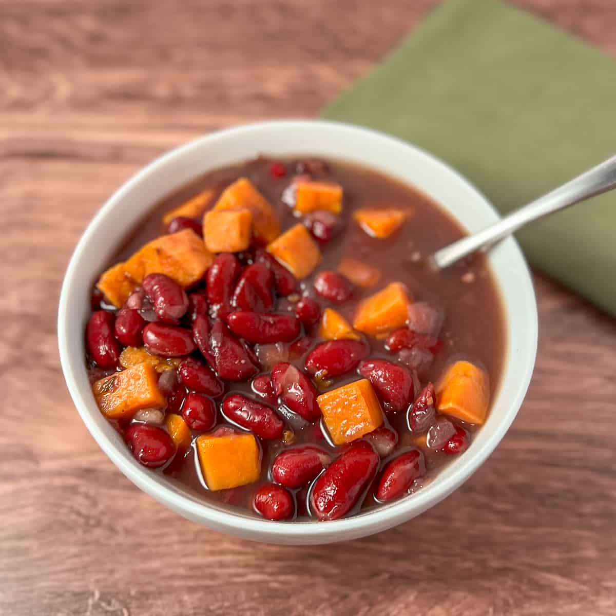top view of red kidney bean soup with sweet potatoes in a white bowl with spoon