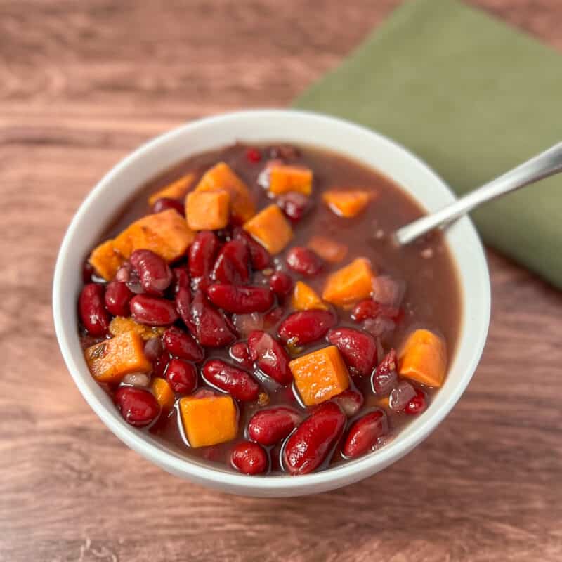 Top side view close up of red kidney bean soup with sweet potato in a white bowl with spoon and green napkin on the side