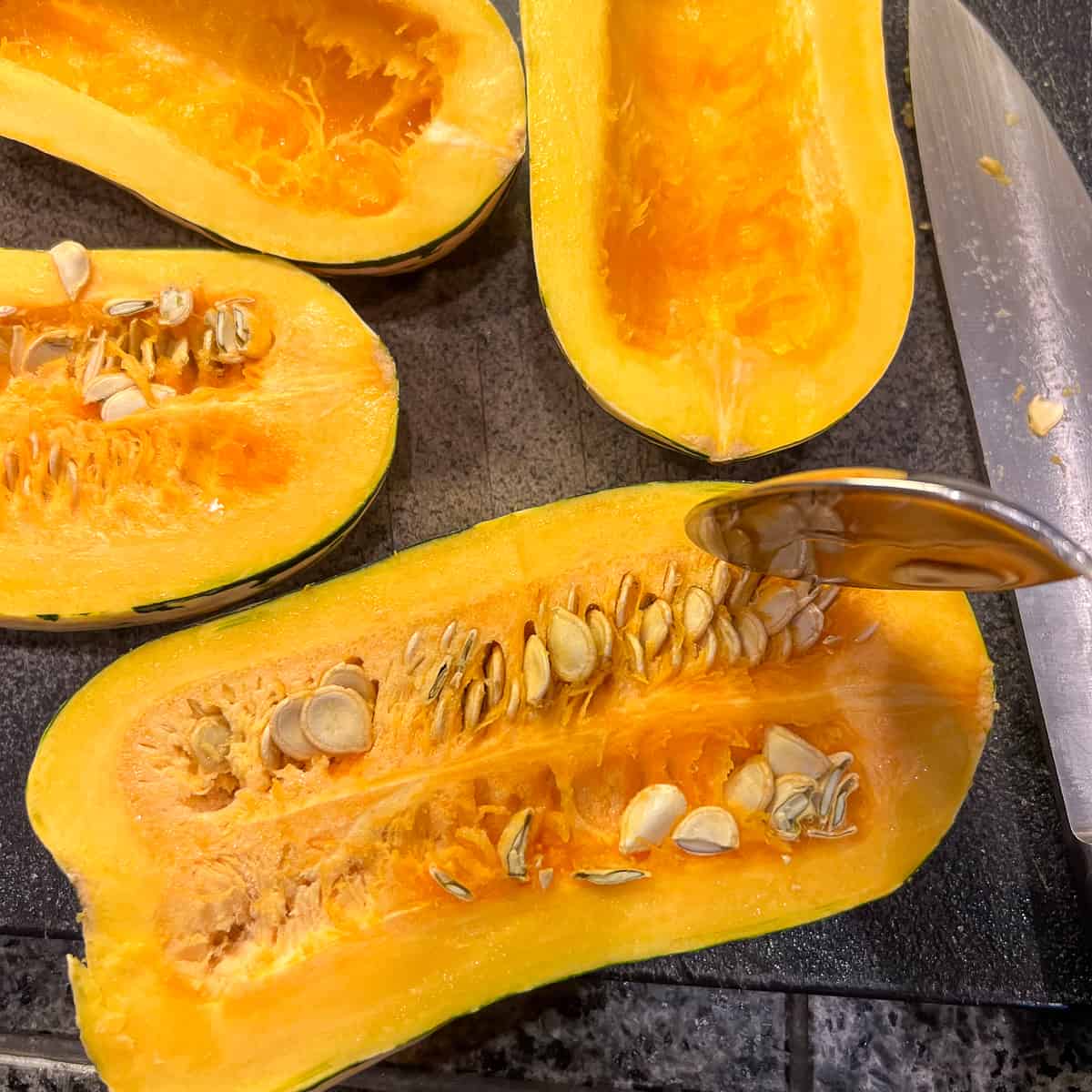 top view of delicata squash halves being deseeded with a spoon