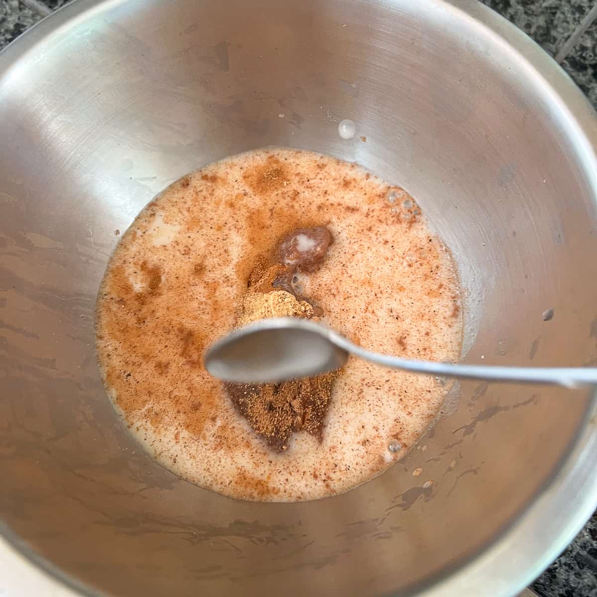 top view of a mixing bowl with a slurry of arrowroot powder, water, date syrup and spices; spoon in position to stir it