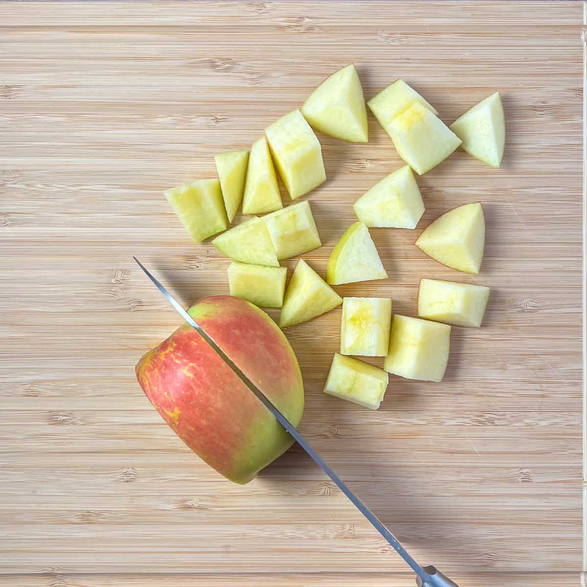Apples being chopped with a knife on a cutting board.