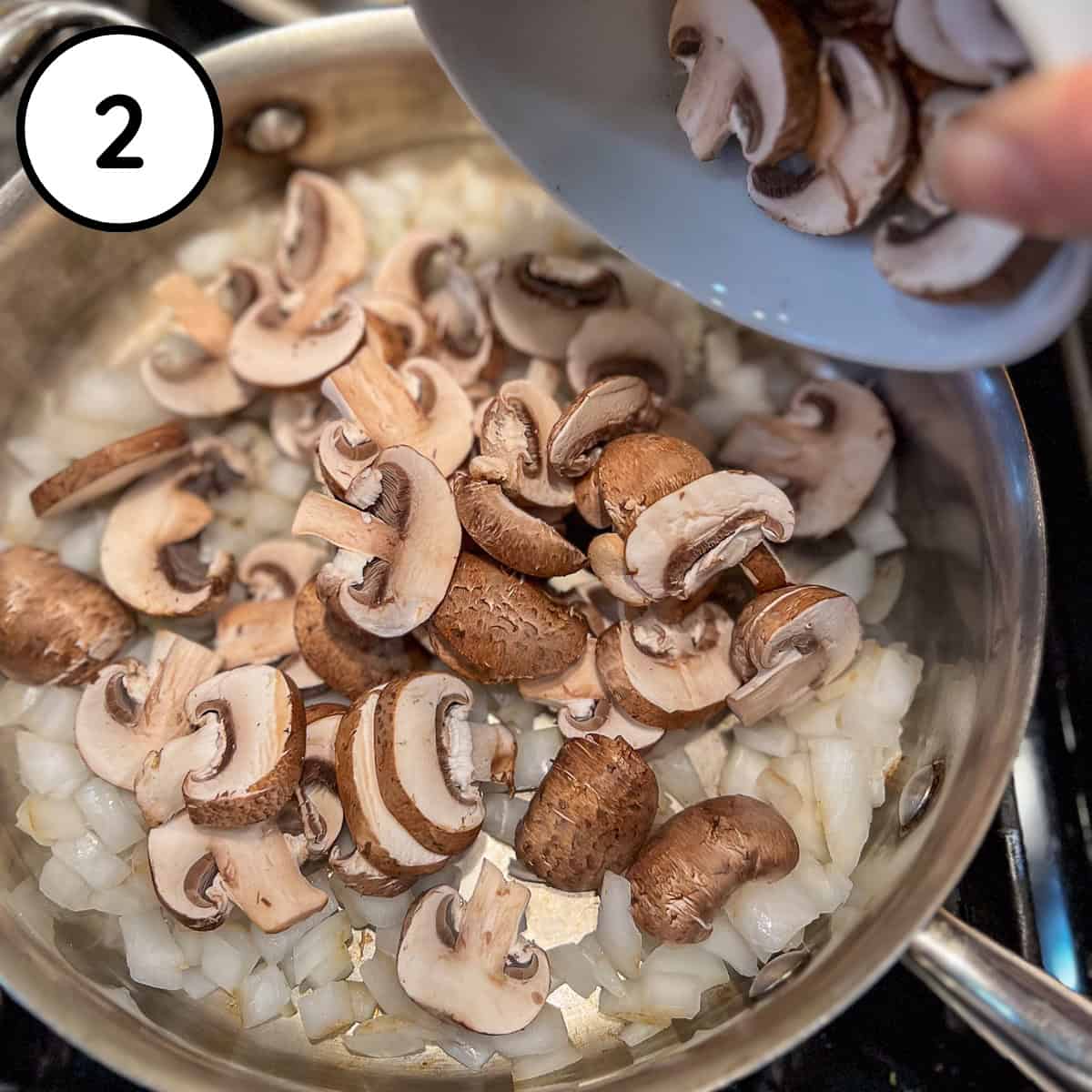 Sliced mushrooms being added to the pan with onions.