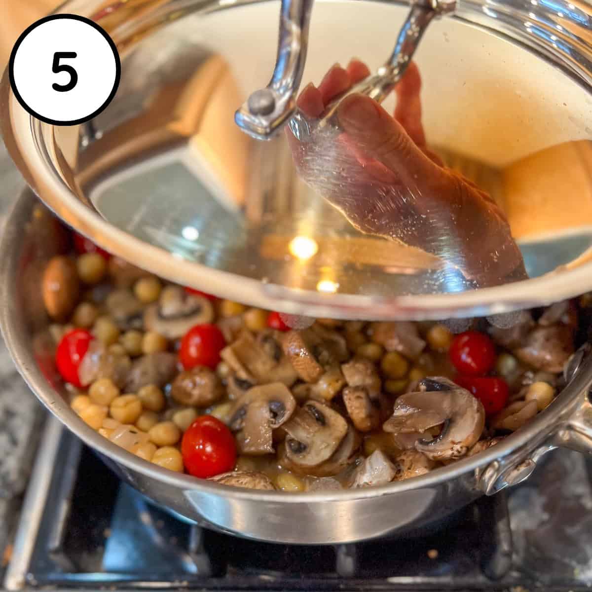 A lid being added to pan with mushrooms, chickpeas, tomatoes and miso-broth.