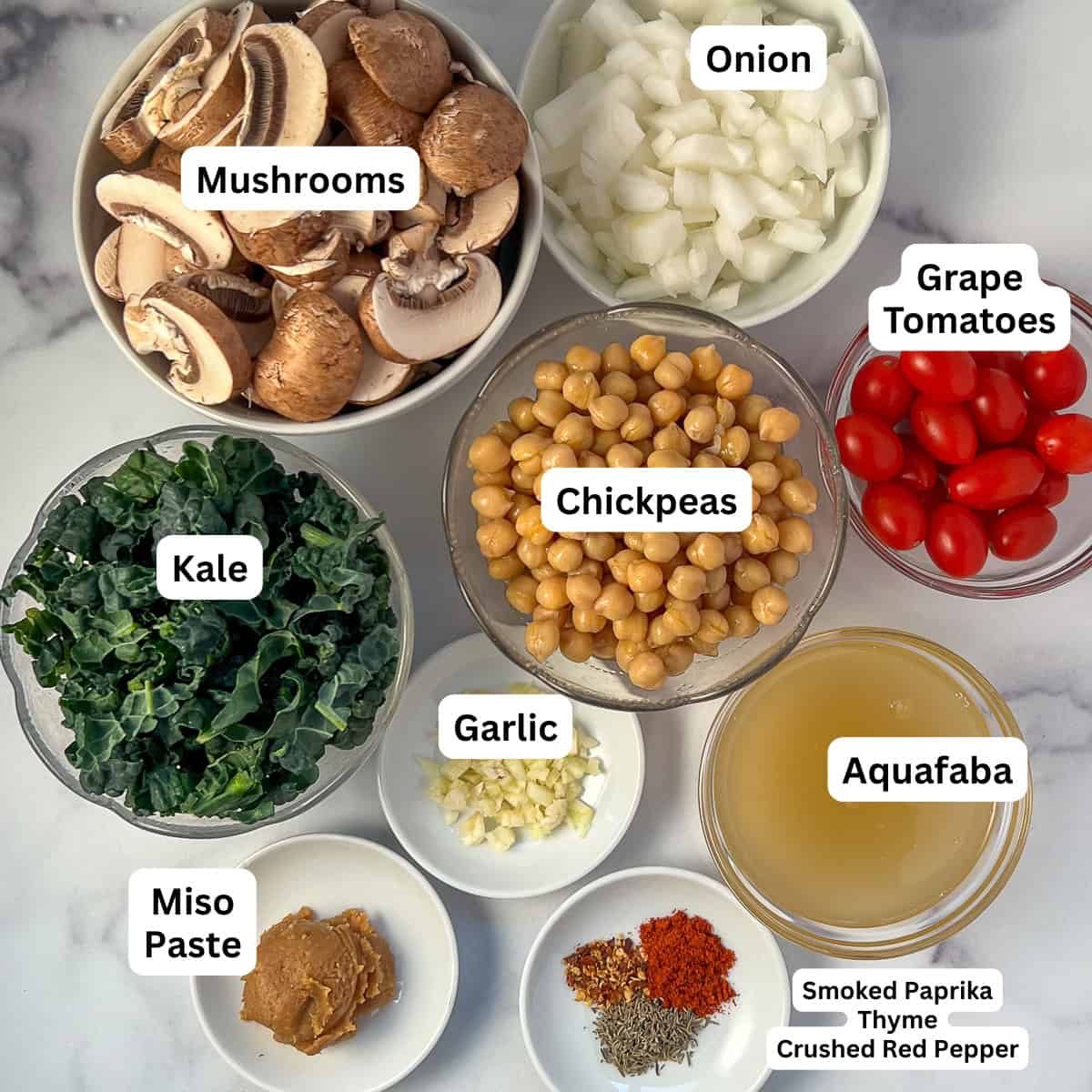 Ingredients for chickpea and mushroom stew: mushrooms, onion, chickpeas, garlic, tomatoes, kale, aquafaba, miso paste, and spices.
