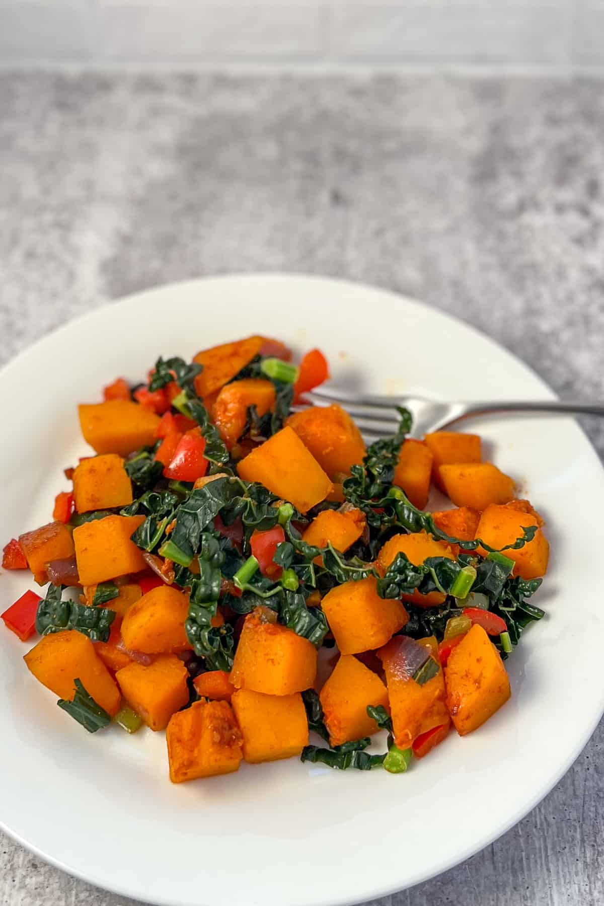butternut squash breakfast has with kale and red bell pepper on a plate with fork on the side