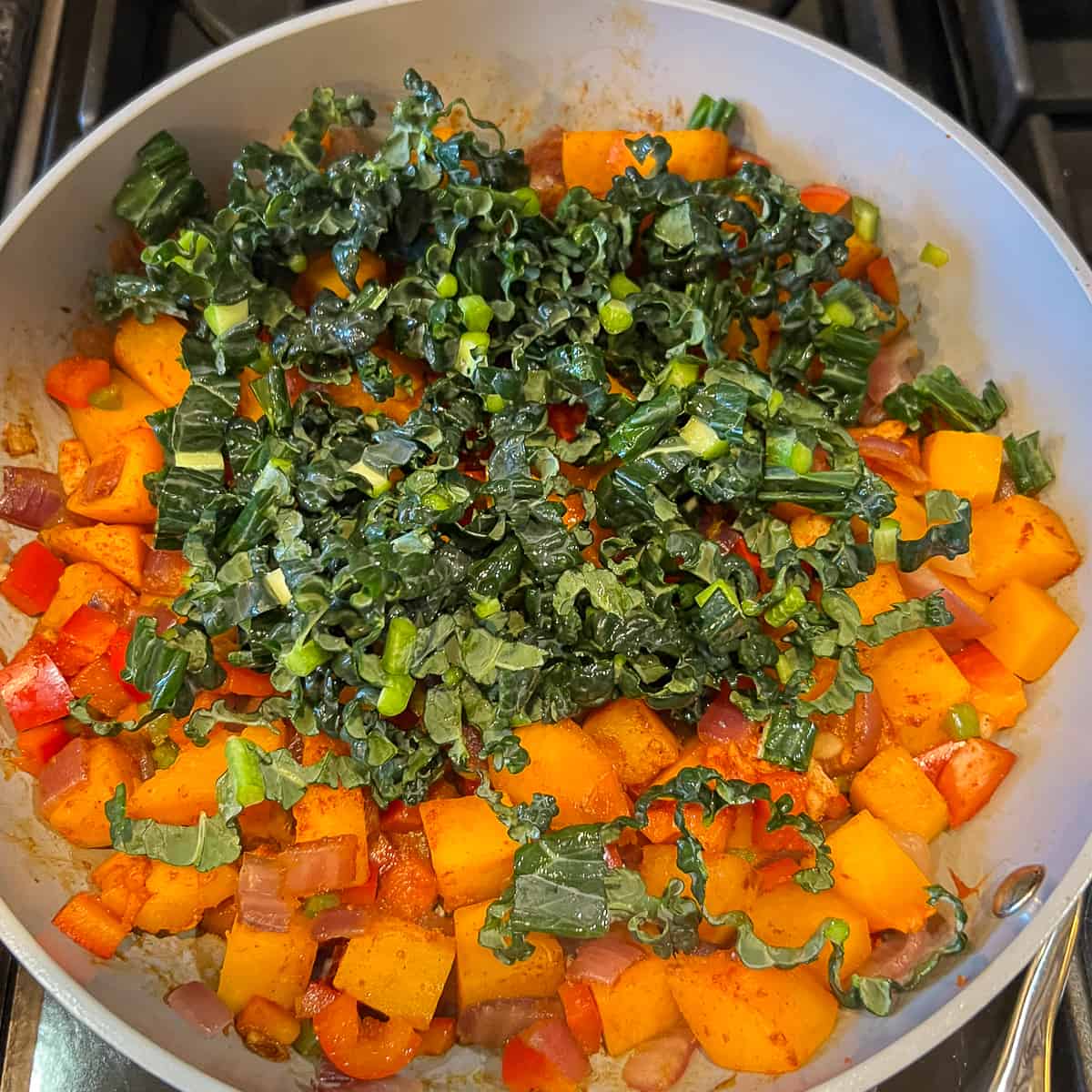 A pan with chopped kale, butternut squash cubes and other veggies. 