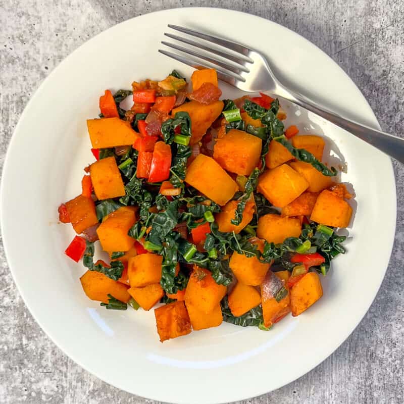 A plate of butternut squash breakfast hash with kale and peppers with fork on the side.
