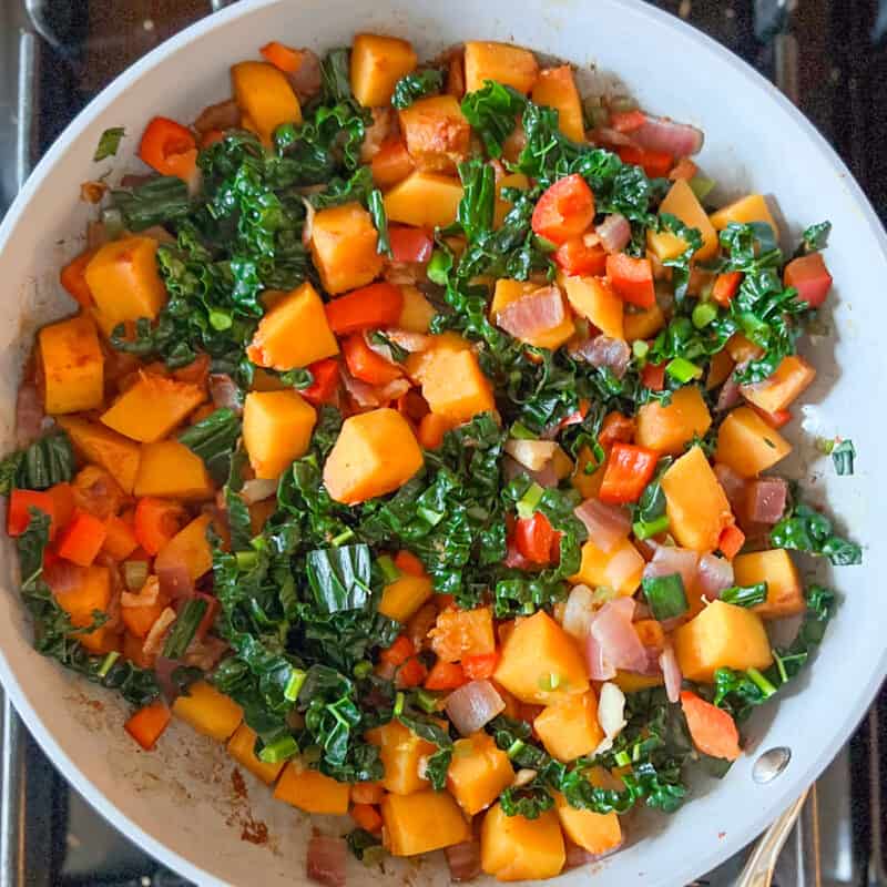 Butternut squash hash with kale and peppers in a pan on the stovetop.