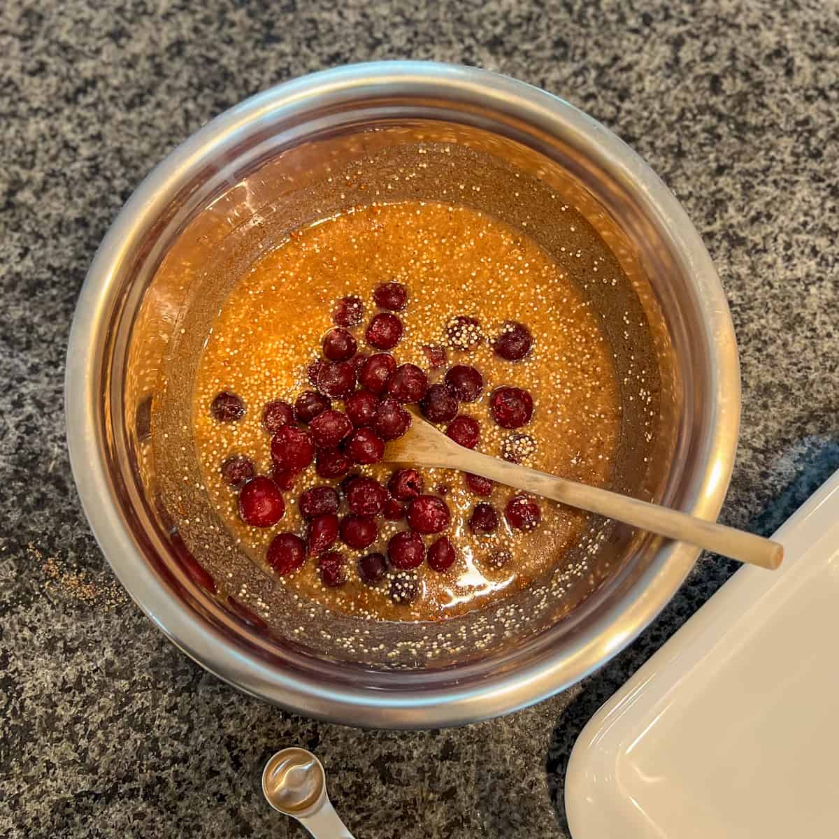 A large stainless steel mixing bowl with cherries, water, quinoa and other ingredients.