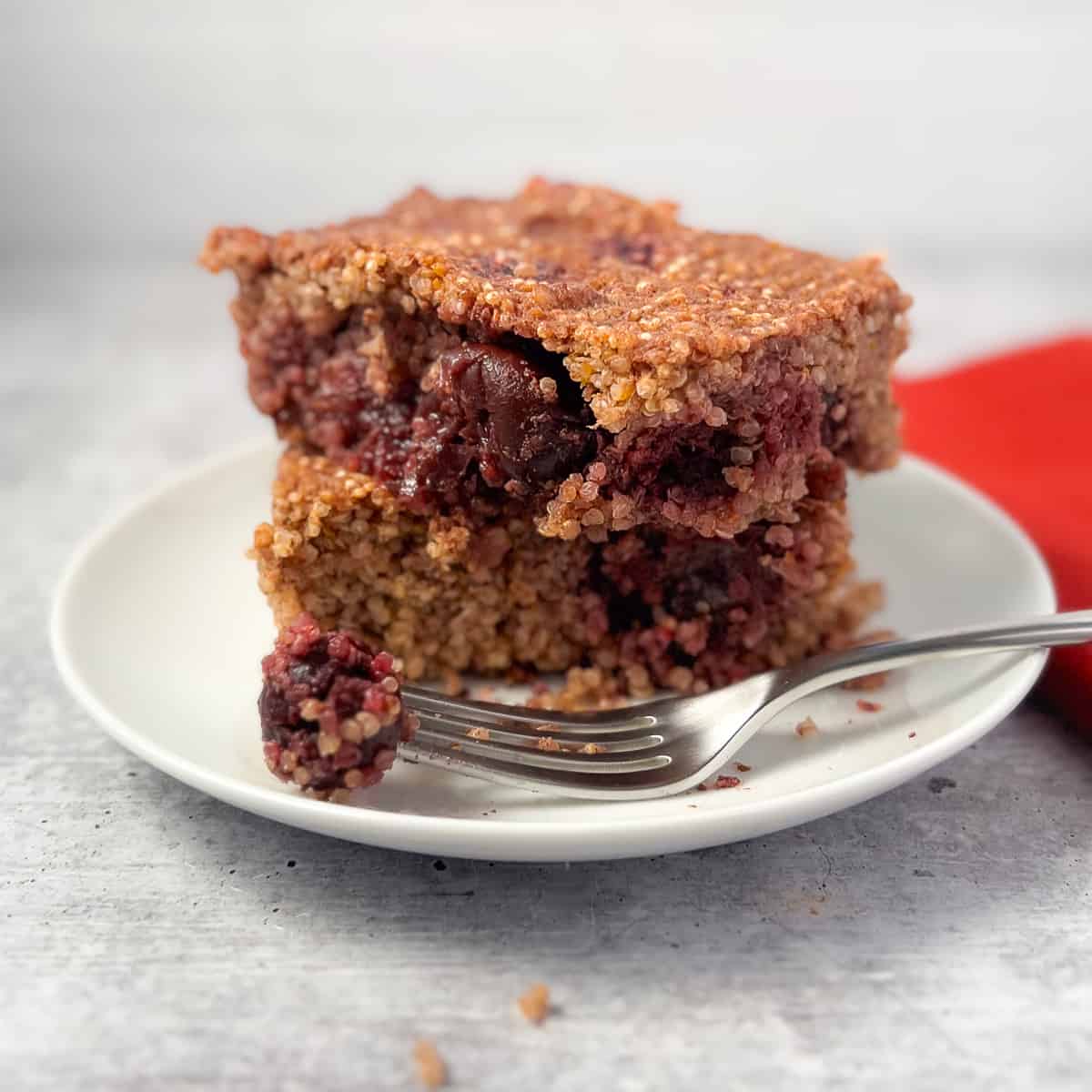 Two stacked slices of cherry quinoa breakfast bake on a plate with a fork on the side.