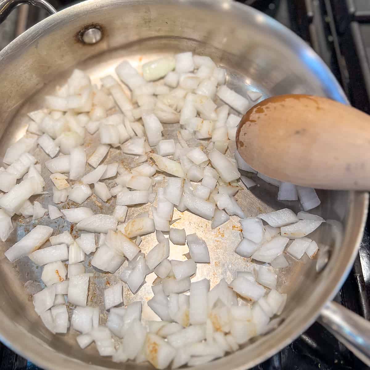 top view of chopped onions in a sauté pan being stirred with wooden spoon