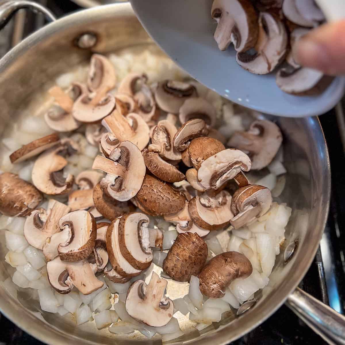 top view of mushrooms being added to the saute pan with onions