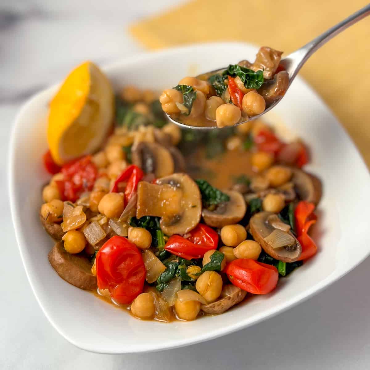 top side view close up of miso chickpea and mushroom stew with tomatoes and kale in a bowl; spoon lifting some out of the bowl