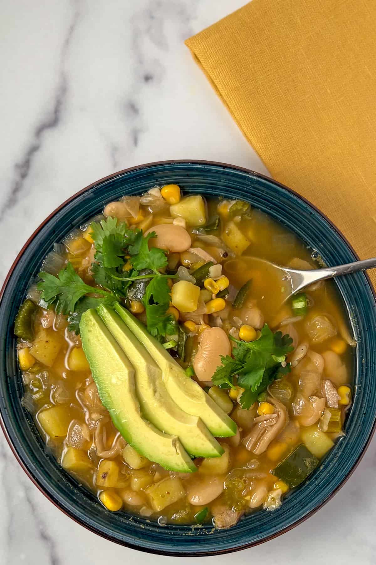 Bowl of white bean chili with sliced avocado and fresh cilantro on top.