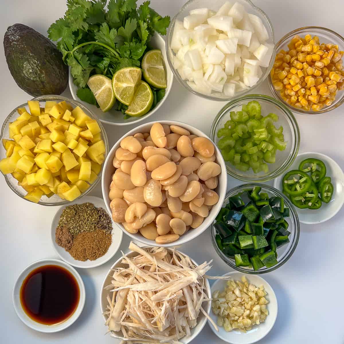 The ingredients for vegan white bean chili: butter beans, shredded oyster mushrooms, diced potatoes, chopped onion, corn, chopped celery, chopped peppers, minced garlic and herbs and spices.